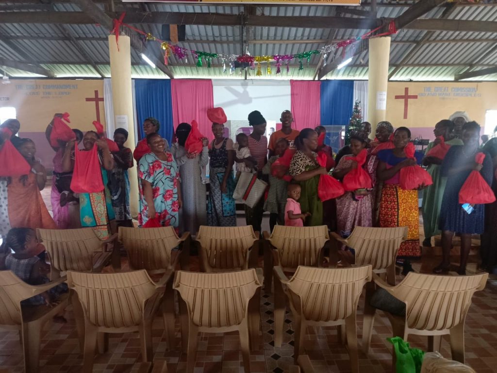 Frauen in der Tiwi-Kirche halten ihre roten Lebensmittelpakete, die während der Weihnachtsaktion 2024 verteilt wurden.